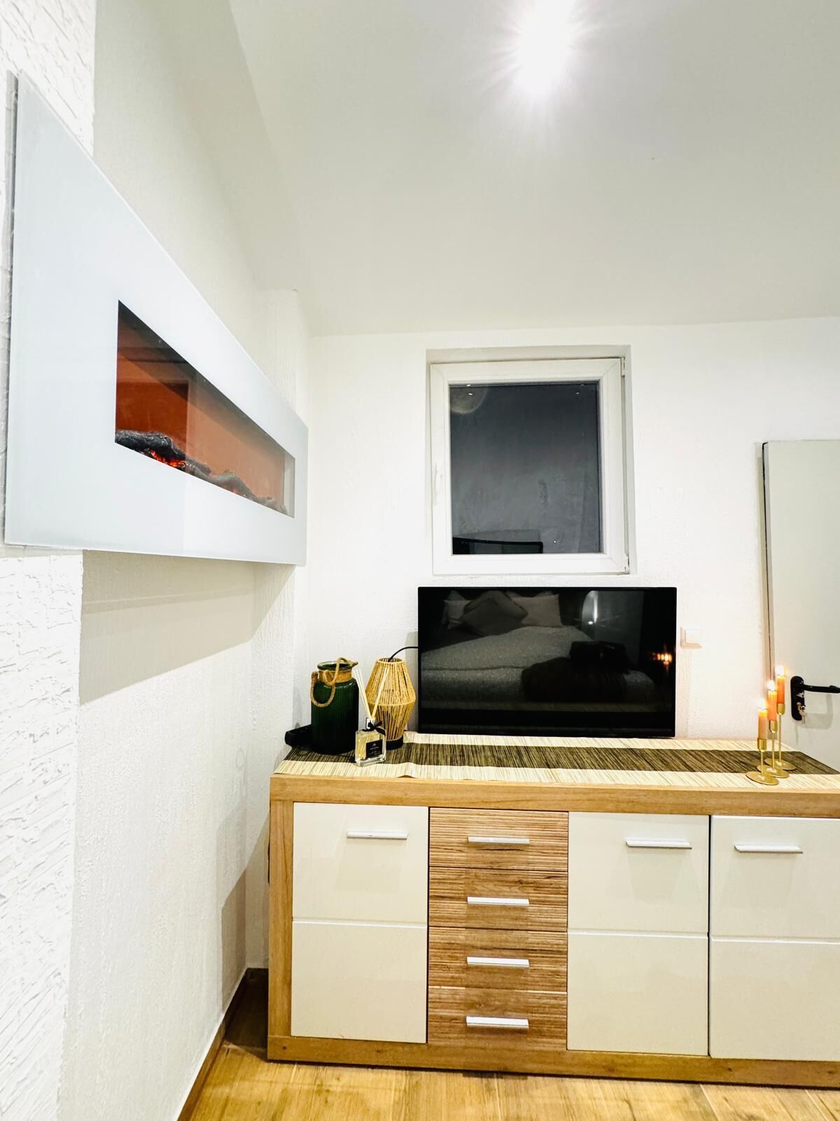Una habitación moderna con un mueble de madera, un televisor de pantalla plana sobre una ventana y un espejo en la pared.