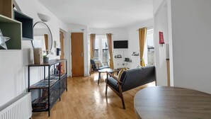Una sala de estar moderna con piso de madera, una mesa de comedor redonda, un sofá y un televisor montado en la pared.