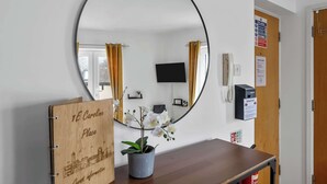 Habitación de hotel con un espejo grande y redondo, un letrero de madera, una orquídea en maceta, una mesa de madera y un televisor montado en la pared.
