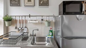 Una cocina con un lavamanos de acero inoxidable, un microondas Kenwood y utensilios colgantes.