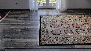 Une pièce spacieuse dotée d’une grande porte-fenêtre coulissante donnant sur un balcon, d’un tapis à motifs sur le sol, d’une horloge murale et d’un tableau encadré.