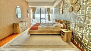 A bedroom with a bed, a dresser, a nightstand, a mirror, and a view of the city through large windows. - Premium Vacation Home in Old Dubai  (Dubai)
