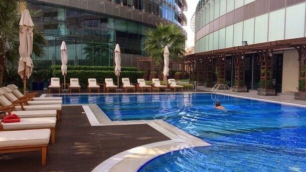 A swimming pool with lounge chairs and umbrellas, surrounded by modern buildings. - Premium Vacation Home in Old Dubai  (Dubai)