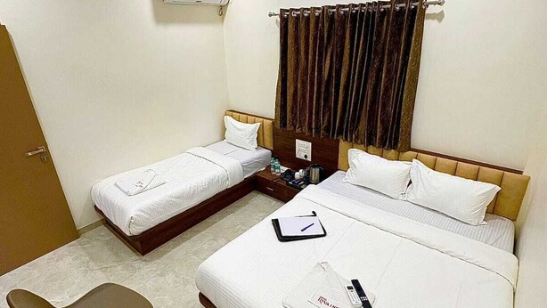 A hotel room with two single beds, a desk, a chair, a ceiling fan, and an air conditioning unit. - HOTEL RIVA INN (Miraj)