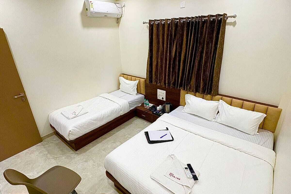A hotel room with two single beds, a desk, a chair, a ceiling fan, and an air conditioning unit.