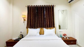 A hotel room with a bed, a nightstand, a lamp, an air conditioner, and a ceiling fan. - HOTEL RIVA INN (Miraj)