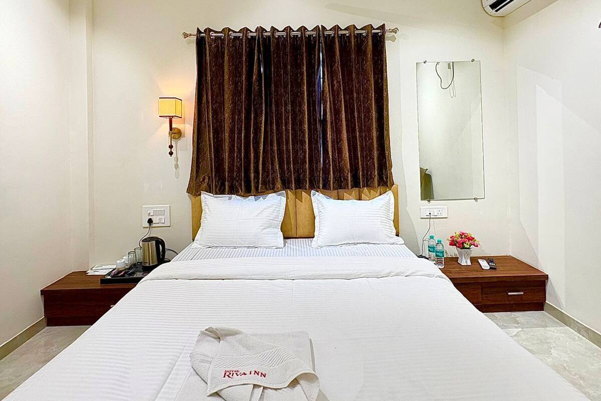 A hotel room with a bed, a nightstand, a lamp, an air conditioner, and a ceiling fan.