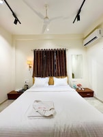 Habitación de hotel con cama, mesita de noche, lámpara, aire acondicionado y ventilador de techo.