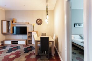 Un salon moderne avec un téléviseur, un meuble de rangement en bois, une table à manger et un tapis à motifs.