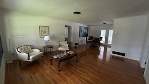 A spacious living room with hardwood flooring, a coffee table, two armchairs, a side table, and a television.