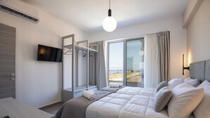 A modern hotel room with a large bed, a TV mounted on the wall, a desk with a remote control, and a window with a view of the beach. - Villa Mino Mare (Mylopotamos)