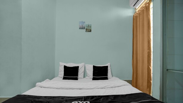 A bed with white and black bedding, a wall-mounted air conditioner, and a window with a brown curtain. - OYO 94908 Demang Kostel (Palembang)