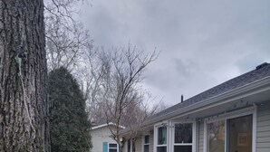 A patio with a table and chairs, a tree, and a house in the background. - Peaceful riverfront home, 3 bedroom,  sleeps 6, in Elkhart. (Elkhart)