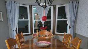 A dining room with a round wooden table, six wooden chairs, a chandelier, and two windows with curtains. - Peaceful riverfront home, 3 bedroom,  sleeps 6, in Elkhart. (Elkhart)