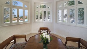 Una sala da pranzo con tavolo e sedie in legno, ampie finestre ad arco e un lampadario.