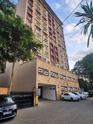 A multi-story building with a flat facade, a gated entrance, and a parking area with several cars. - Beautiful Afro-inspired 1-bedroom 1.5 bathroom apartment in Westlands Nairobi (Nairobi)