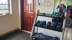 Un'area fitness con una porta in legno, una finestra, un termostato a parete e un supporto per manubri con pesi.