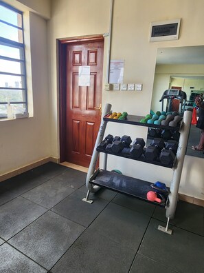 A gym area with a wooden door, a window, a wall-mounted thermostat, and a dumbbell rack with weights. - Beautiful Afro-inspired 1-bedroom 1.5 bathroom apartment in Westlands Nairobi (Nairobi)