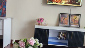 Un soggiorno con un tavolino in vetro, un vaso bianco con fiori, un telecomando e una TV a parete che mostra una scena floreale.
