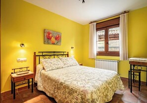 A bedroom with a bed, a nightstand, a table, a window with curtains, and a wall painting. - La Viña Rural Apartments (Apartment number 4) (Cangas de Onís)