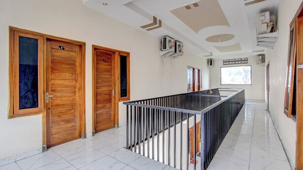 A hallway with wooden doors, a metal railing, and tiled flooring. - OYO 94919 Nay Guesthouse Dan Kost (Surakarta)