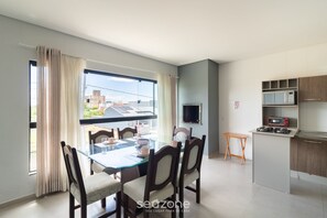 Une cuisine moderne équipée d’un four à micro-ondes et d’une cuisinière intégrés, un coin repas avec une table en verre et des chaises en bois, et une vue sur l’extérieur grâce à de grandes fenêtres.