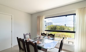 Un coin repas avec une table et des chaises en verre, donnant sur un paysage verdoyant et des bâtiments, le tout visible à travers une fenêtre.