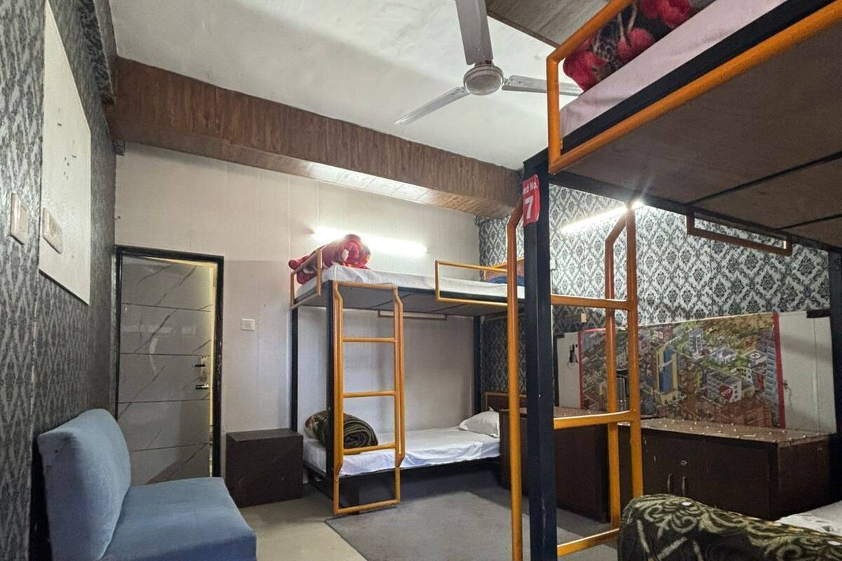 A dormitory room with bunk beds, a ceiling fan, a blue chair, and a patterned wall.