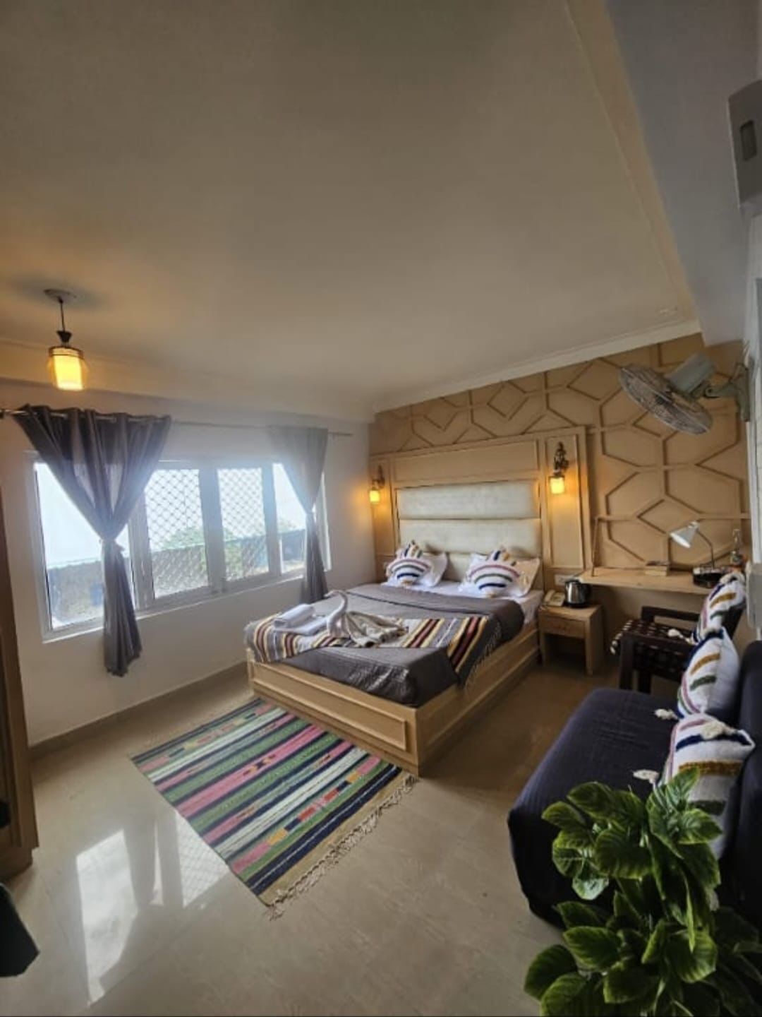 A bedroom with a bed, bedside table, lamp, and a potted plant.