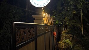Une enseigne portant l’inscription « RAKE N FLOW » est illuminée la nuit, entourée d’une végétation luxuriante.