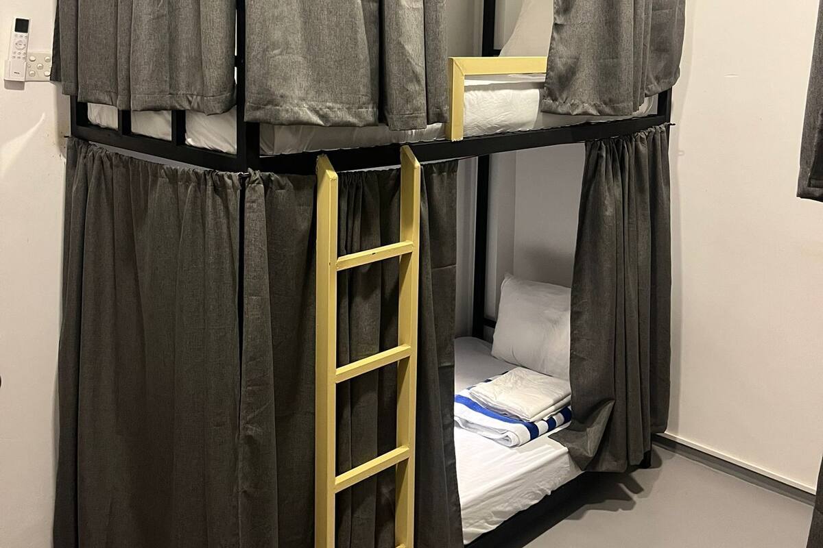 A bunk bed with grey curtains, a wooden ladder, and a white mattress.
