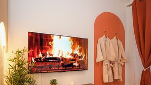 Una sala moderna con un televisor de pantalla plana mostrando una chimenea, una consola de madera con una planta y un par de batas colgadas en un perchero de pared.