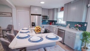Een moderne keuken met grijze kastjes, een centraal eiland met blauwe placemats, en een eethoek met grijs beklede stoelen.