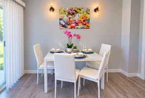 Un comedor con una mesa de vidrio, sillas blancas y un cuadro en la pared.