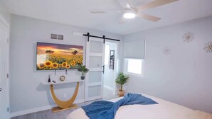 Een slaapkamer met een bed, een plafondventilator, een televisie, een raam en een deur.