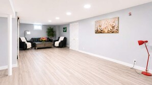 Ein geräumiges Zimmer mit hellem Holzboden, einer schwarzen Ledersofa, einem Couchtisch, einer roten Stehlampe und einem Gemälde an der Wand.