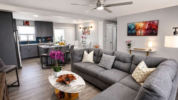 Een moderne woonkamer met een grijze bank, een marmeren salontafel en een plafondventilator.