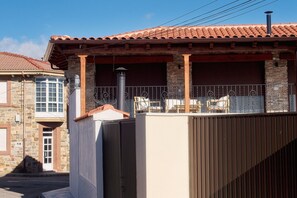 Un edificio residencial con techo de tejas, balcón con barandilla y fachada de piedra.