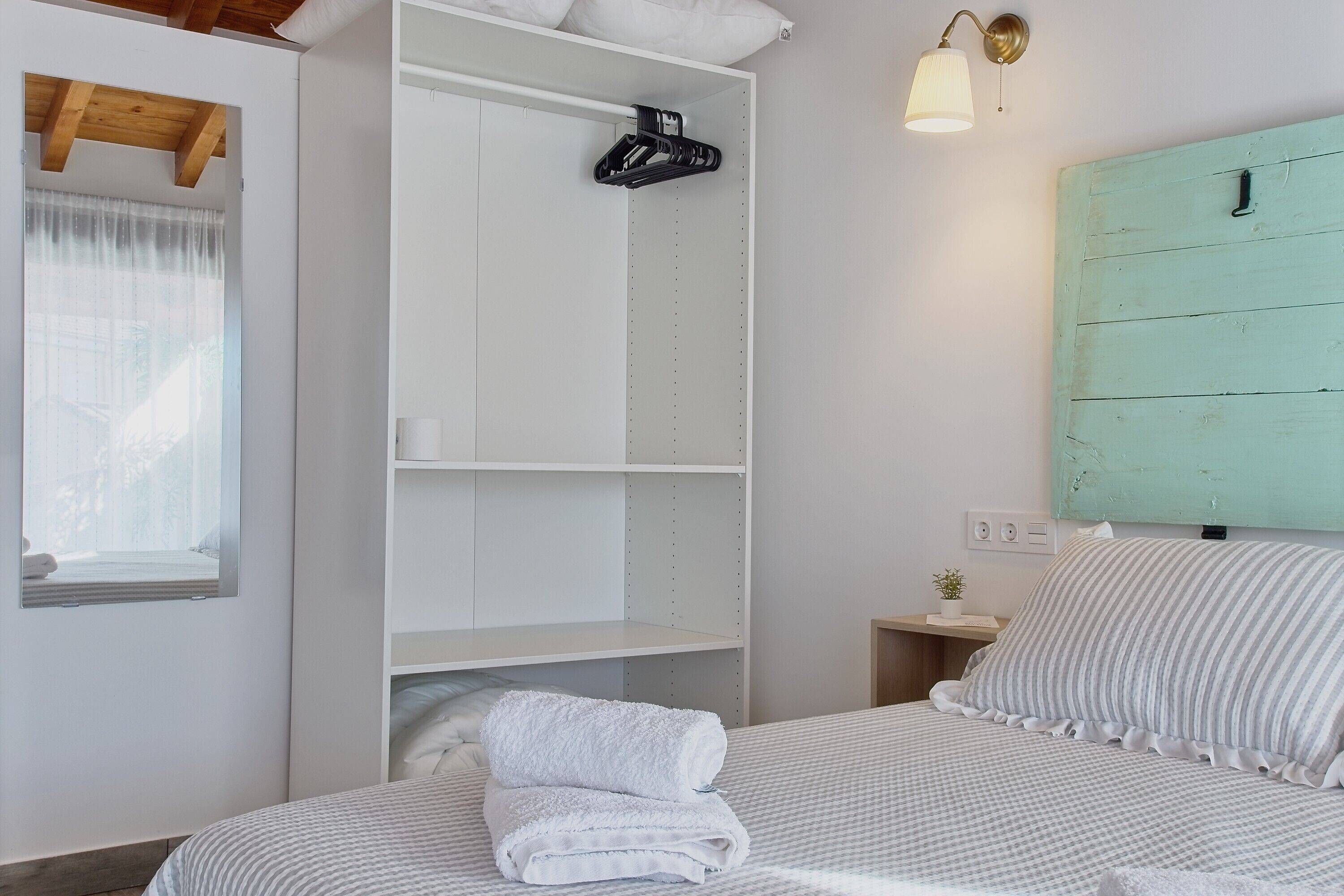 Un dormitorio con cama, armario blanco, mesita de noche pequeña, ventana con cortinas y cabecero verde.