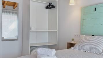 Un dormitorio con cama, armario blanco, mesita de noche pequeña, ventana con cortinas y cabecero verde.