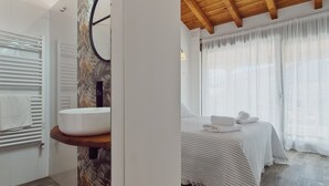 Ein Badezimmer mit einem weißen Waschbecken, einem Spiegel und einem Handtuchhalter. Der Raum verfügt über Holzböden und ein Fenster mit Vorhängen.
