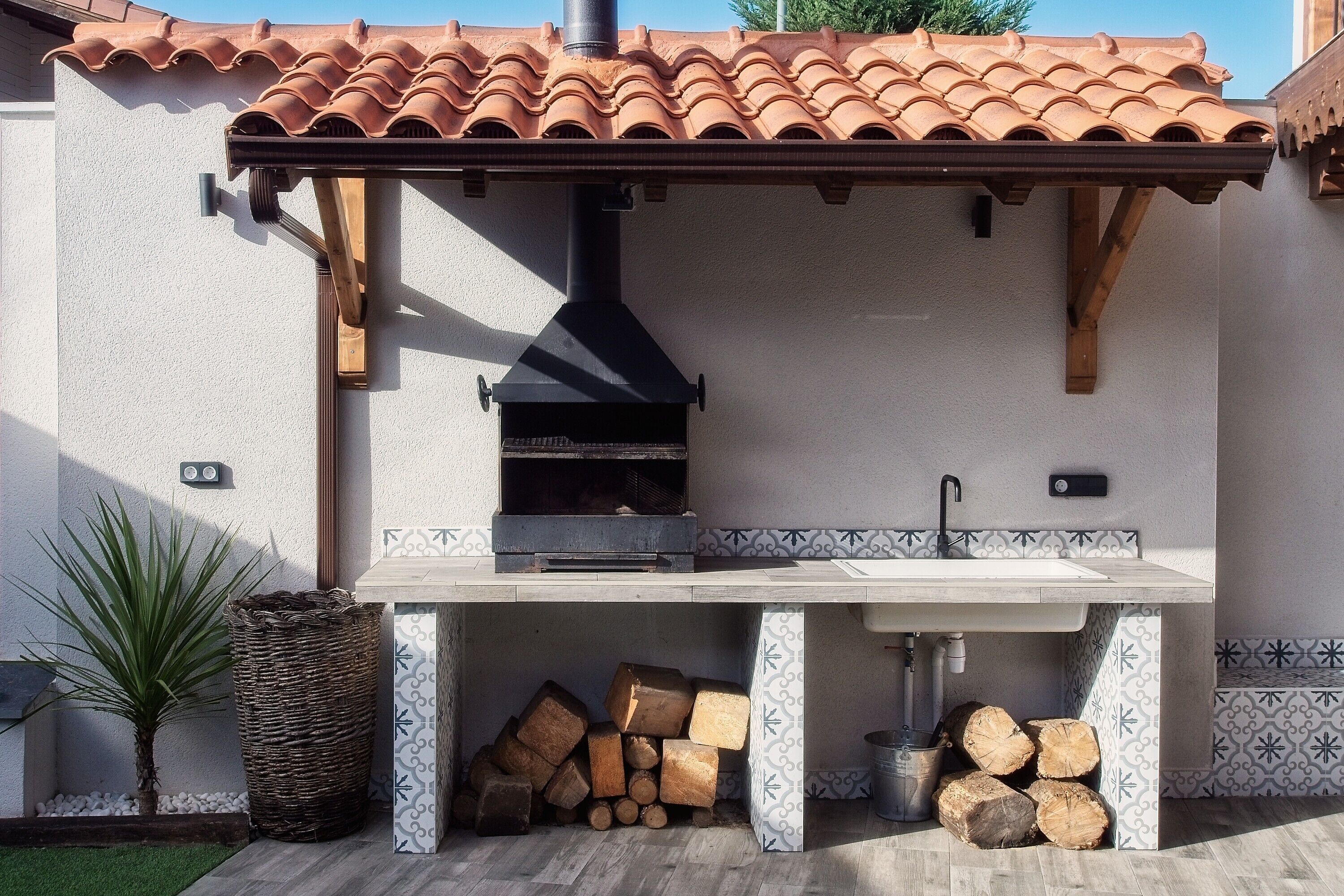 An outdoor kitchen with a chimney, a sink, and a tiled backsplash.
