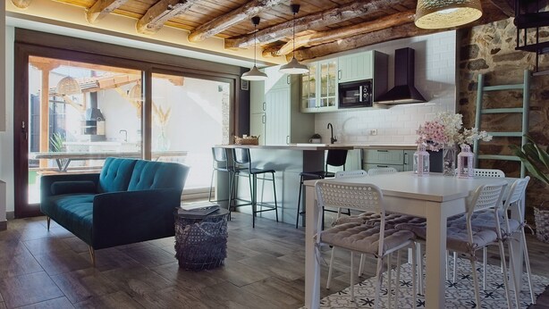 Eine moderne Küche mit Steinwand, Holzbalkendecke und einem Essbereich mit weißem Tisch und Stühlen.