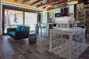 Une cuisine moderne avec un mur en pierre, un plafond en bois et un coin repas comprenant une table et des chaises blanches.