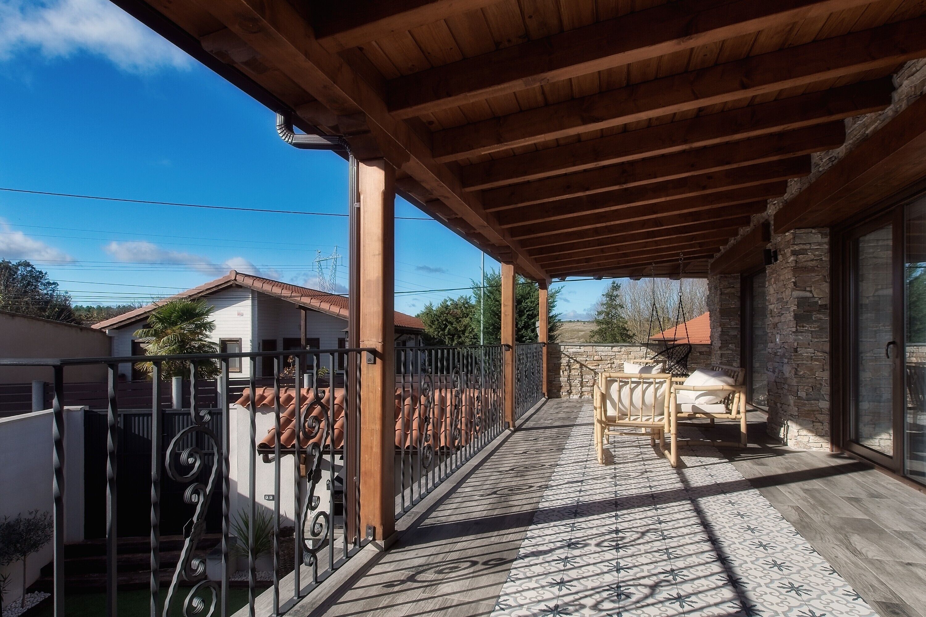 A covered outdoor area with a wooden ceiling, a stone wall, and a patio with a patterned floor.