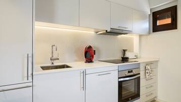 Una cocina moderna con armarios blancos, un lavaplatos de acero inoxidable, un hervidor rojo y un horno.