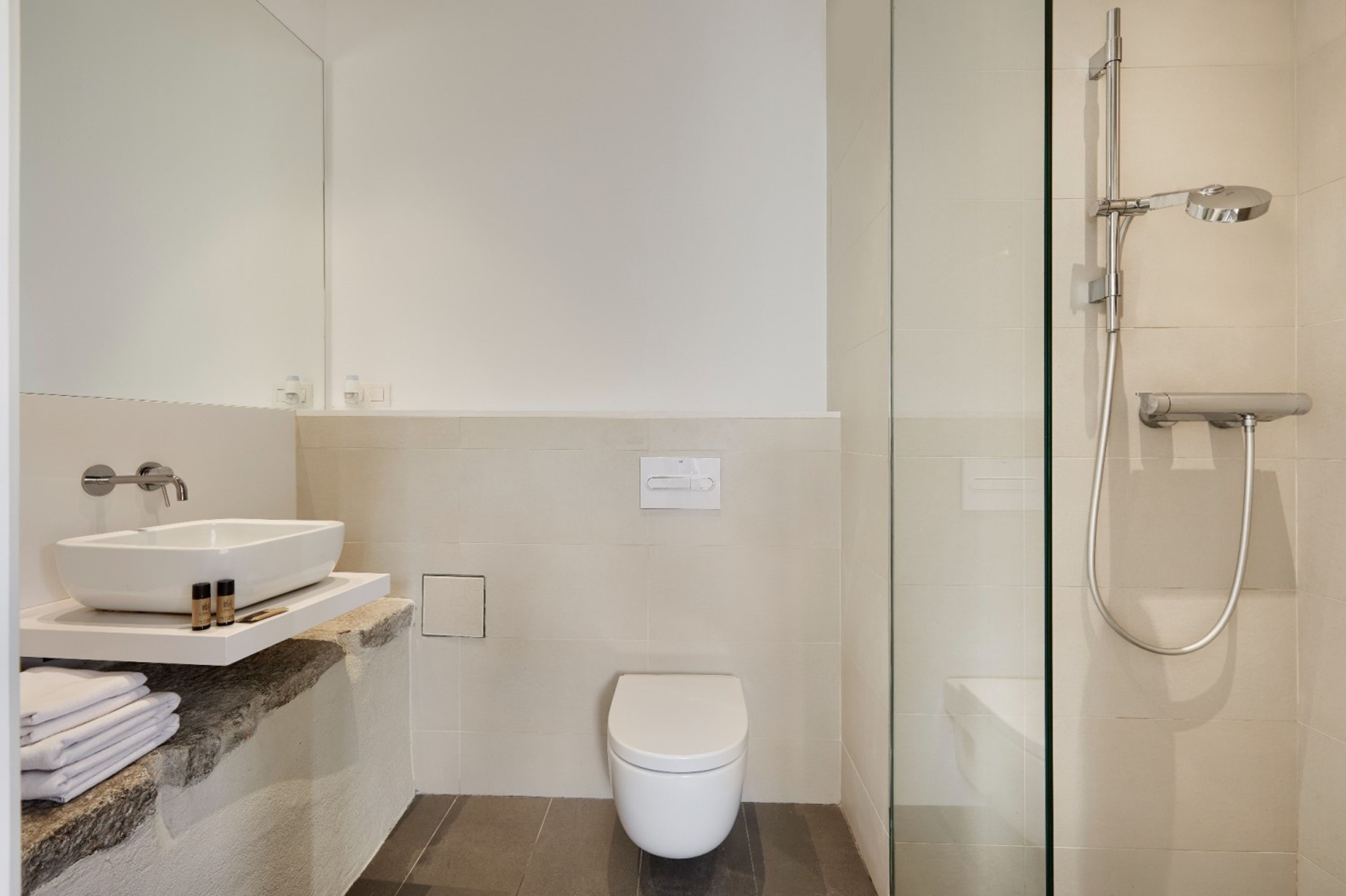 Un baño moderno con un lavamanos blanco, un inodoro y una zona de ducha con mampara de vidrio.