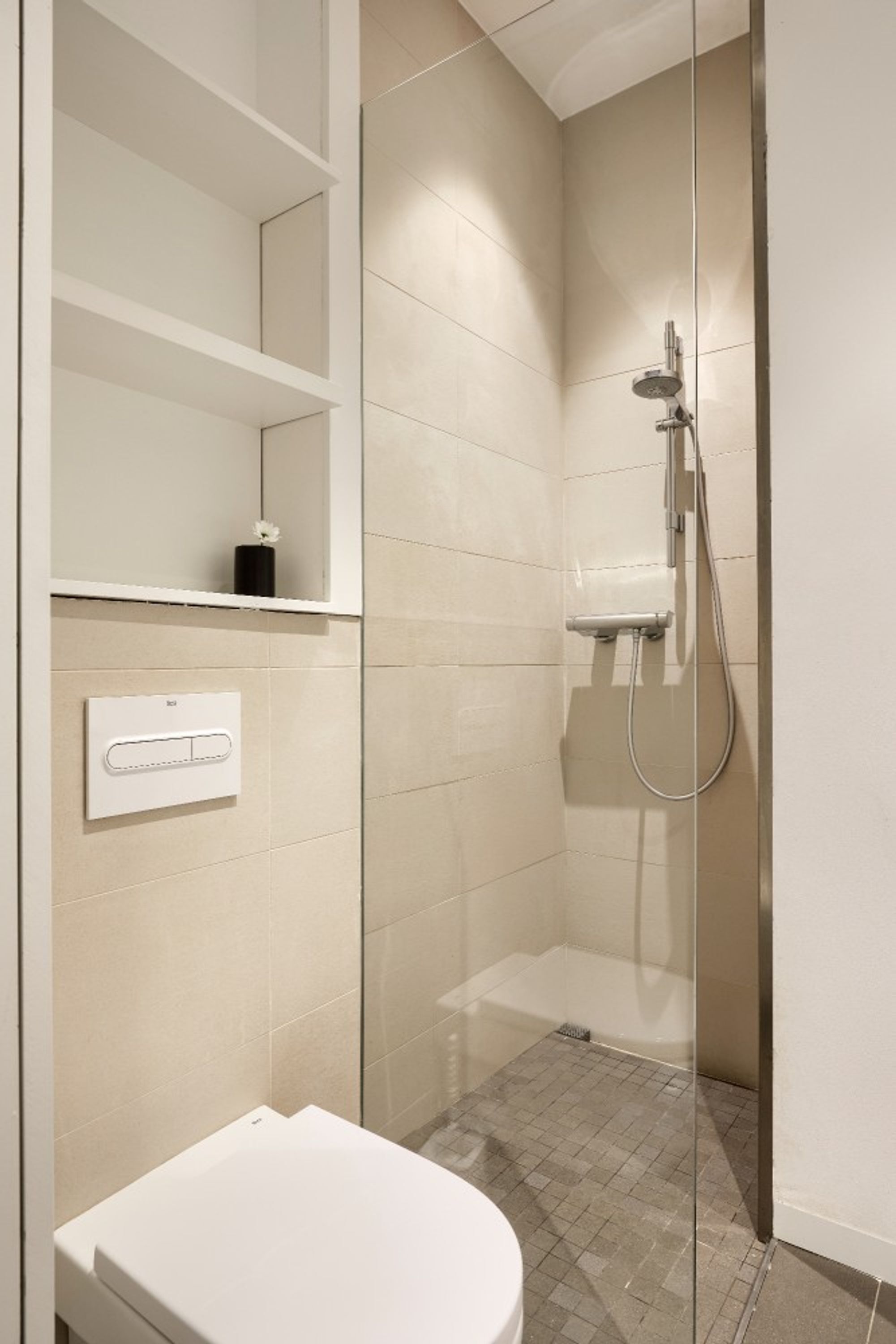 Een moderne badkamer met een douchecabine van glas, een toilet en een inbouwkastje met een kleine vaas.
