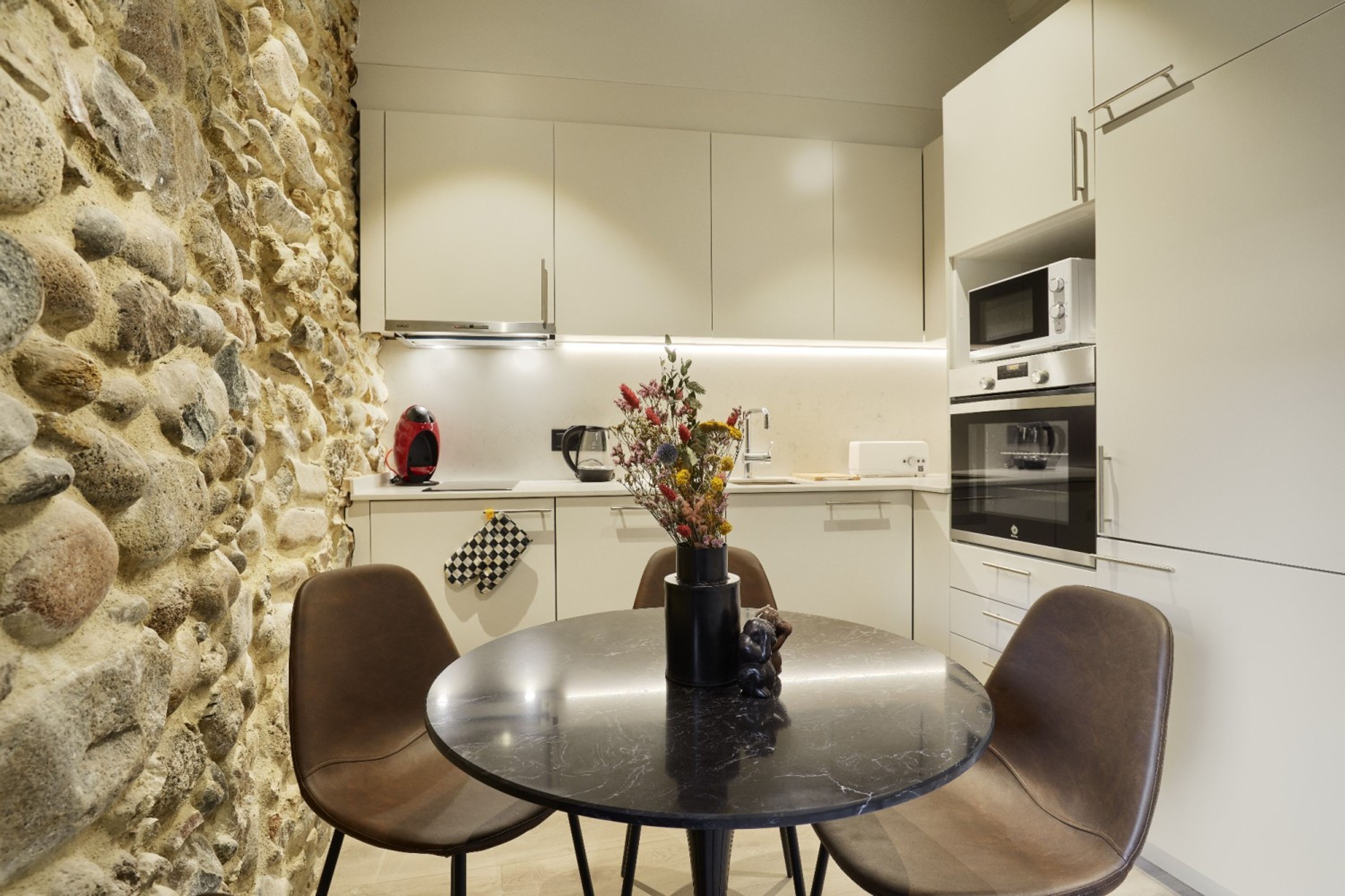 Une cuisine avec un mur en pierre, une table ronde entourée de chaises et des appareils électroménagers modernes.