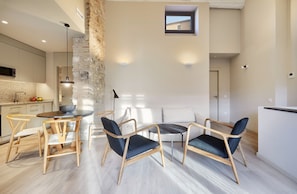 A modern kitchen with a stone accent wall, a dining area with wooden chairs and a round table, and a small window above the seating area. - Casa Calma & Casa Canvas (Girona)